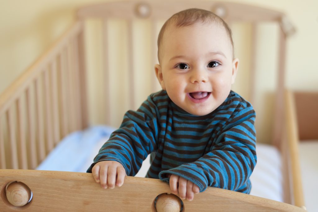 Close-up of a baby smiling and standing in a crib